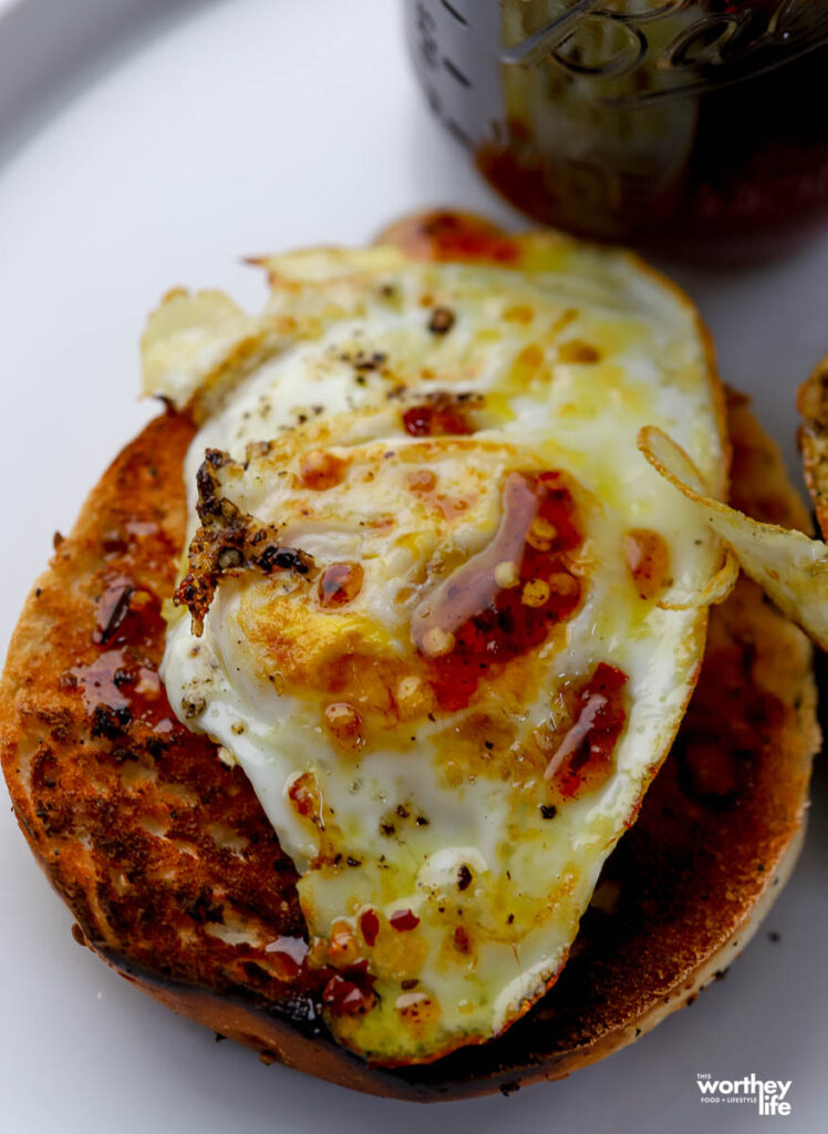 a bagel topped with a fried egg with a drizzle of hot honey on top. 