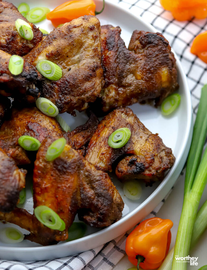 A white plate with jerk chicken wings with scallion and peppers. 