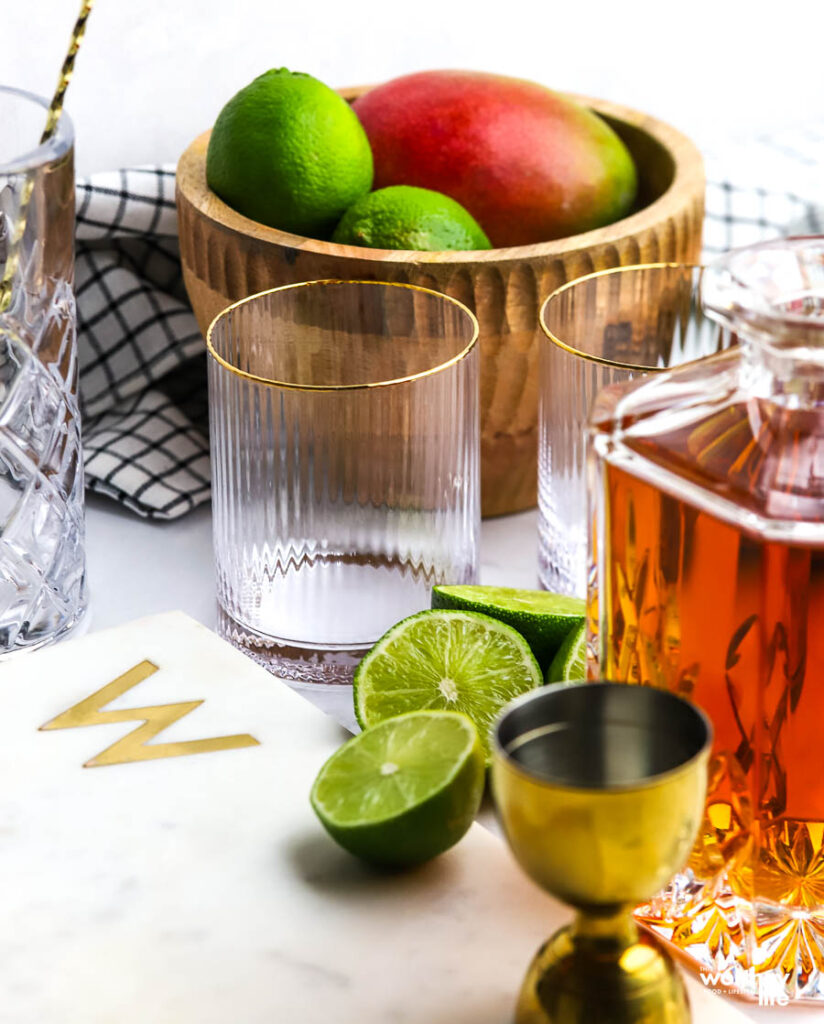 Fresh limes, mango, and whiskey cocktail ingredients for making a mango sour. 