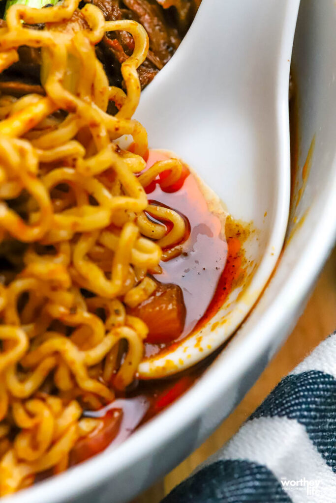 a soup spoon with birria broth and ramen noodles