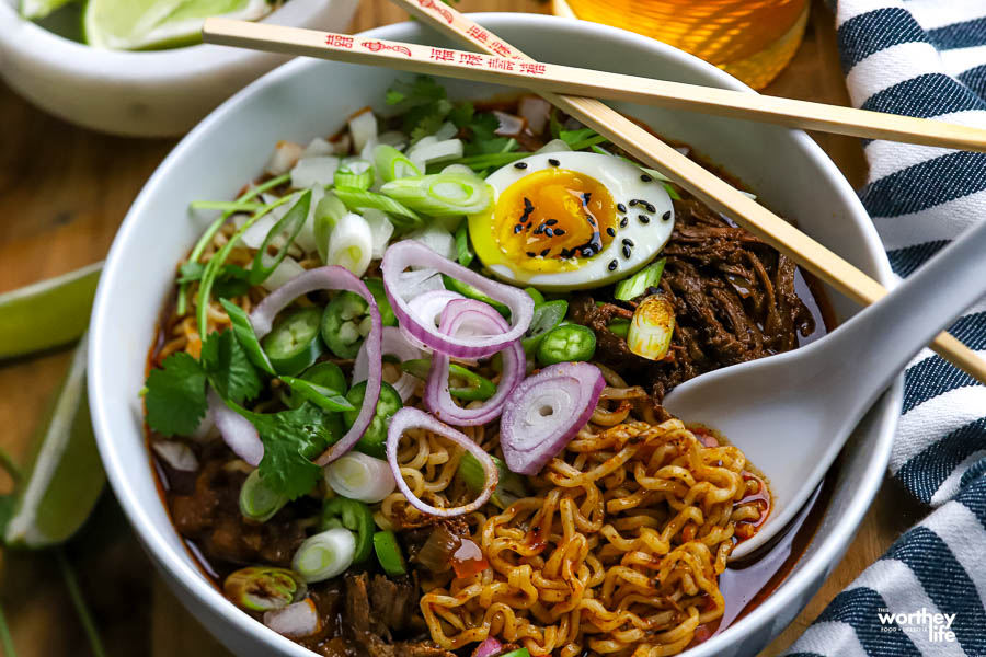  a serving bowl filled with Mexican ramen, with a spoon and wooden chopsticks.