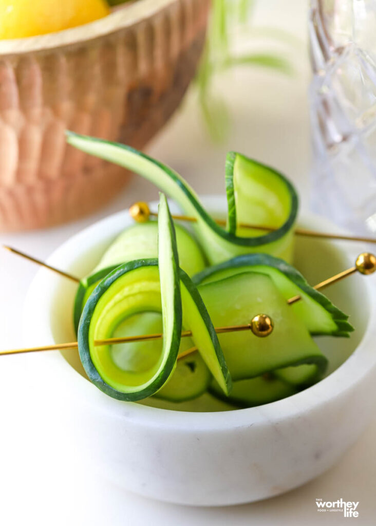 Fresh cucumbers wrapped in a cocktail pin laying in a white marble bowl