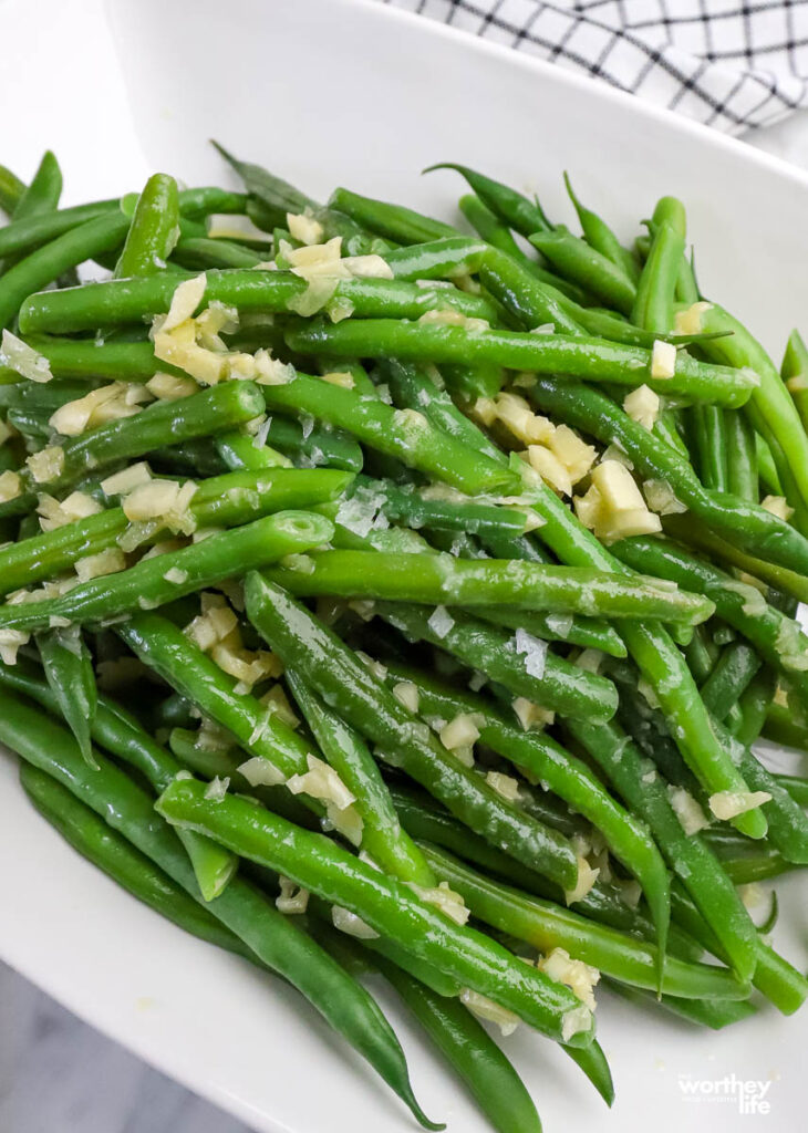 a large white serving bowl filled with green beans. 