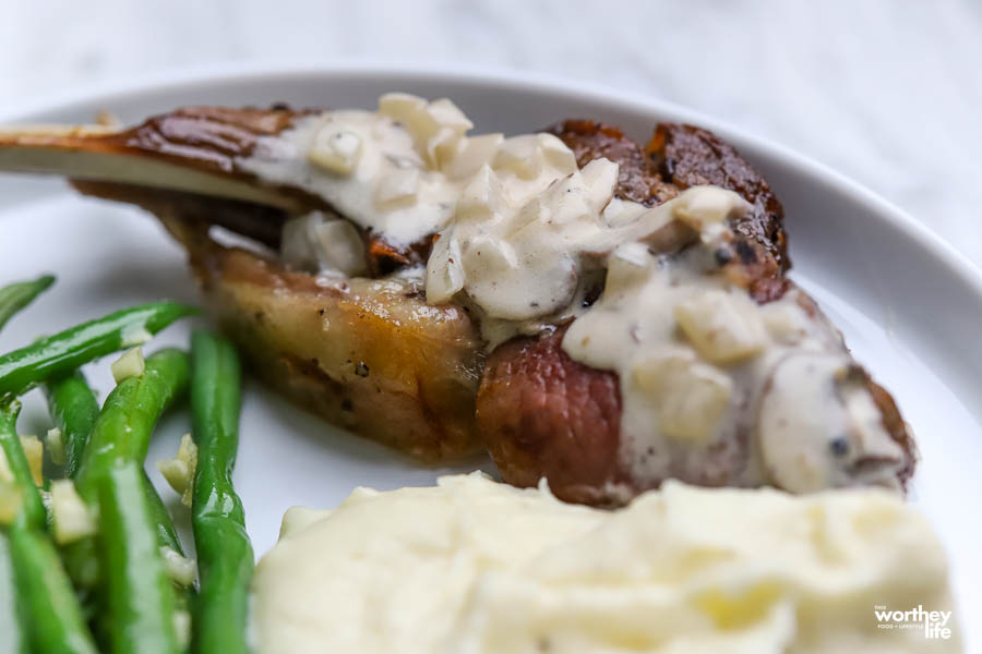 a white dinner plate with lamb, Alfredo potatoes, and honey butter garlic green beans
