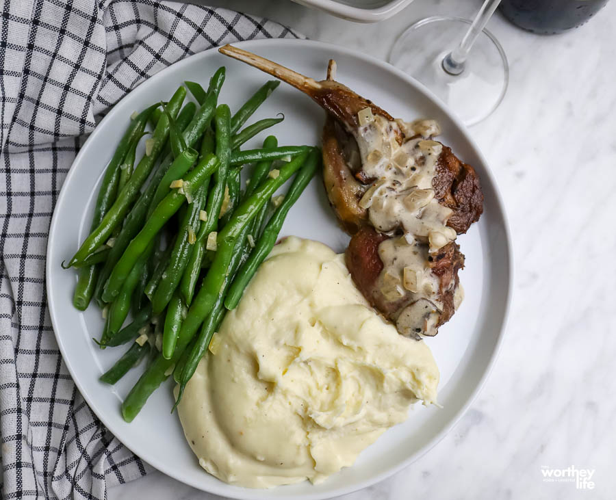 a rimmed white dinner plate with potatoes, lamb, and French green beans