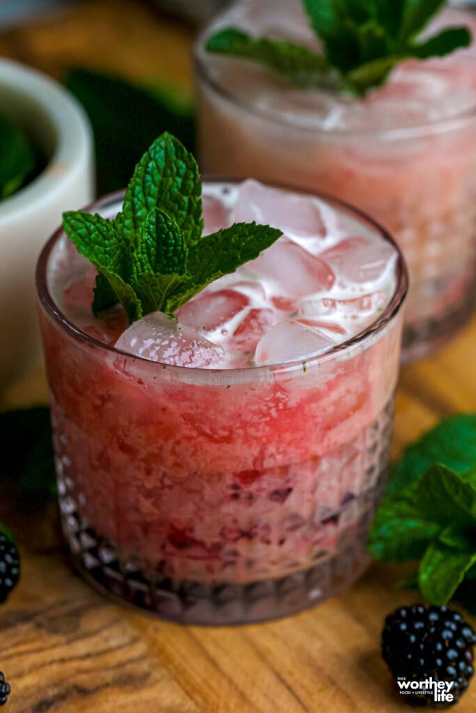 To rocks glasses of our Blackberry Mint Brazilian Lemonade with a mint garnish. 
