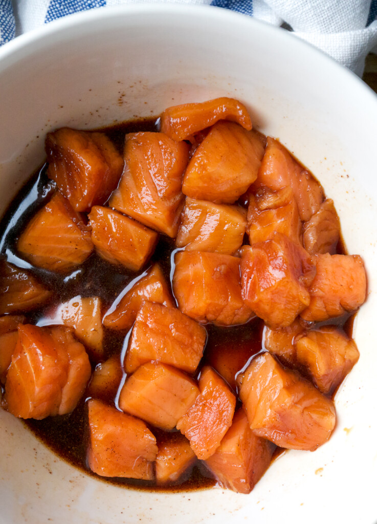 Cubes of salmon soaking in seasoning in a white bowl