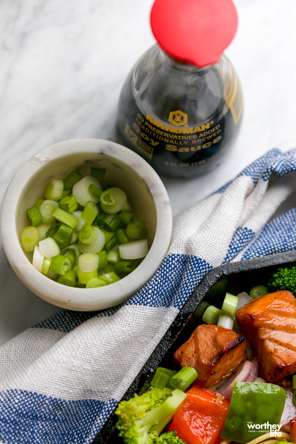 green onions in a white bowl next to a bottle of soy sauce with a red top