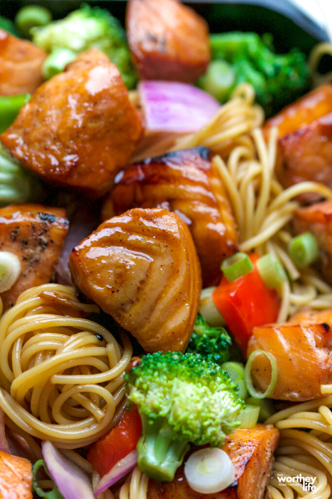 cubes of salmon with soy sauce on them laying next to twirled pasta and veggies