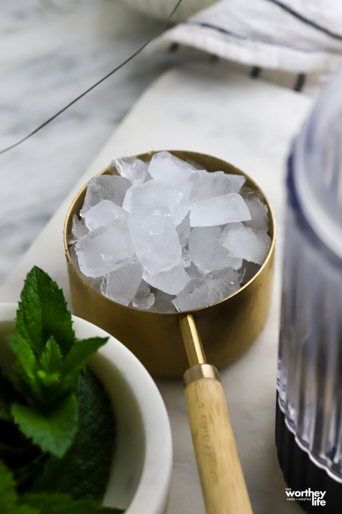 A brass measuring cup with a wood handle filled with pebble ice. 