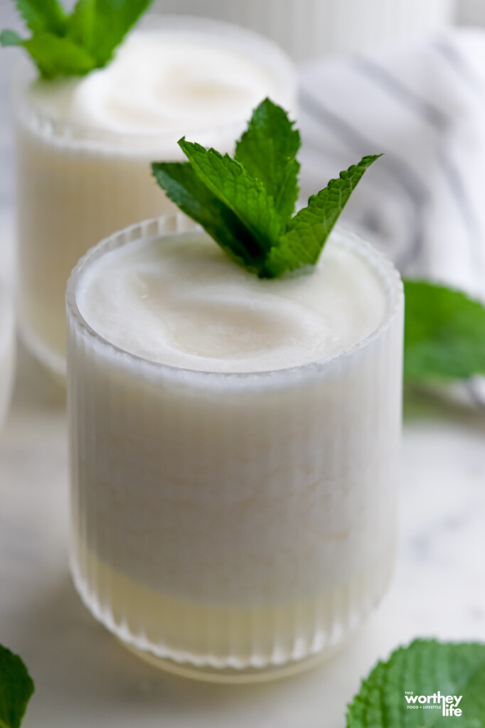 A frozen coconut margarita in a scalloped serving glass topped with fresh mint. 