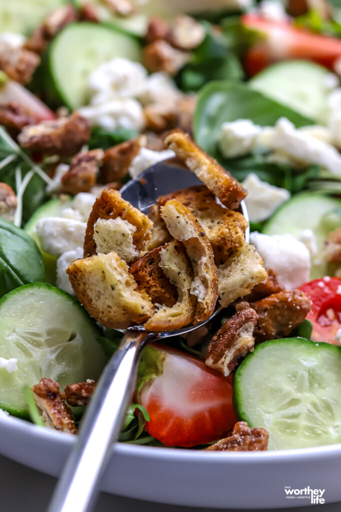 A spoonful of herb bagel bites on a salad.