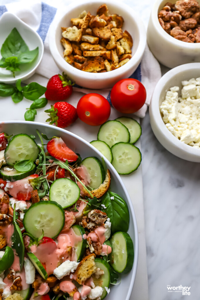 Partial view of a salad in a white serving bowl with raw fresh vegetables on the side.