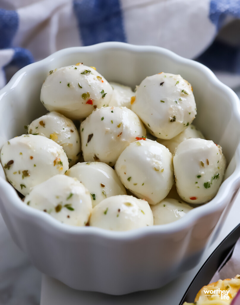 A white fancy bowl filled with small white Mozzarella balls. 