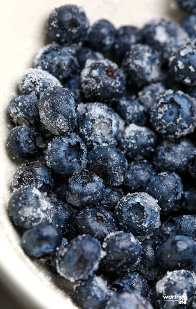 Ripe blueberries tossed with granulated sugar in a large white bowl.