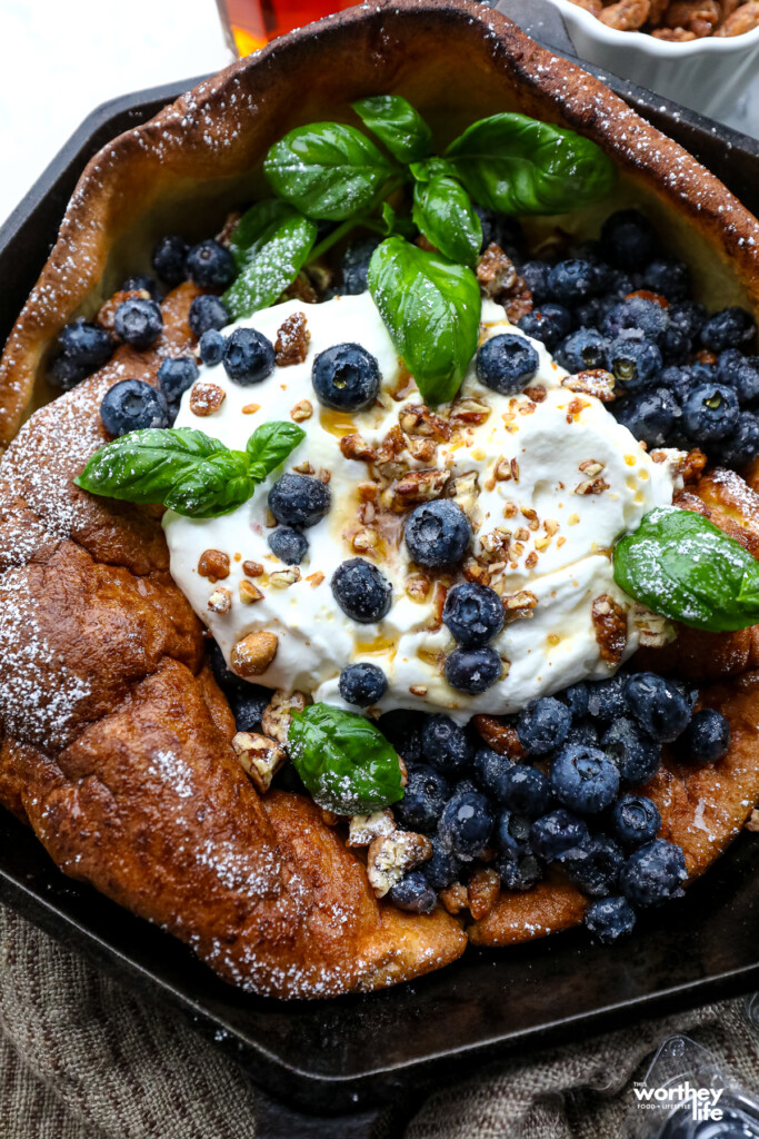 Our blueberry Dutch Baby topped with fresh blueberries tossed with powered sugar, whipped cream, fresh sweet basil, and pecan pralines.
