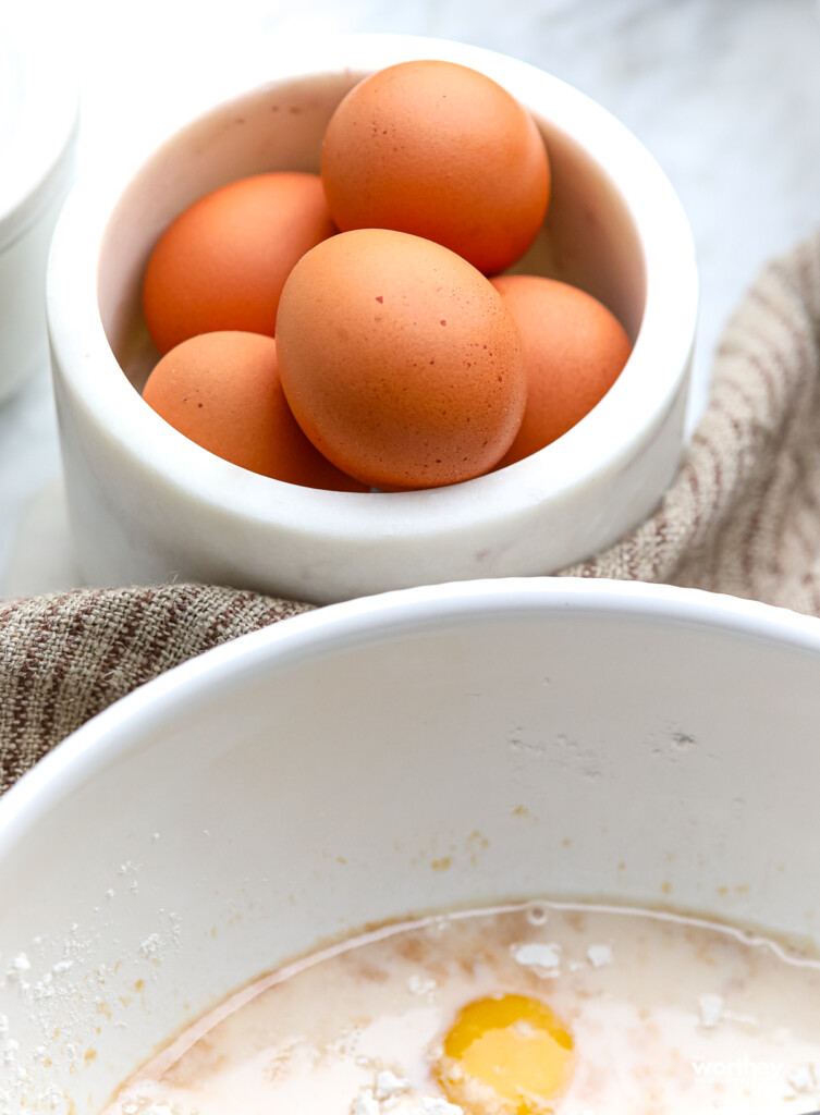 Brown farm eggs in a marble bowl and a white bowl with unmixed ingredients.