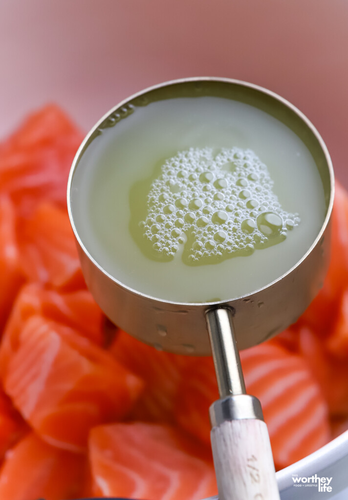 Pineapple juice in a measuring cup and cubes of fresh salmon.