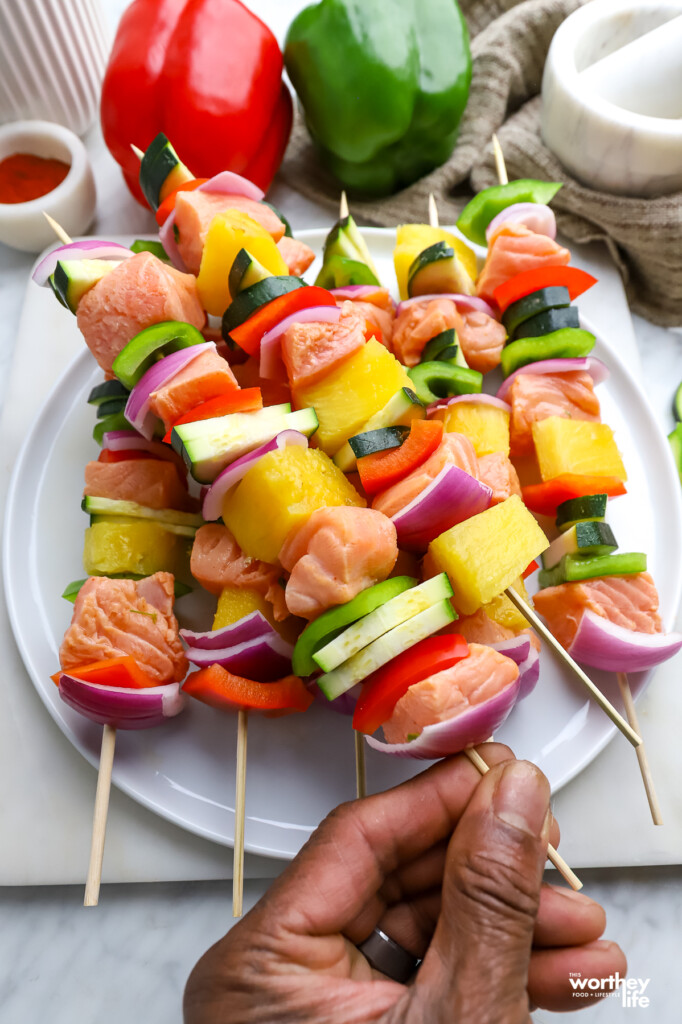 Uncooked kabobs resting on a white platter. 