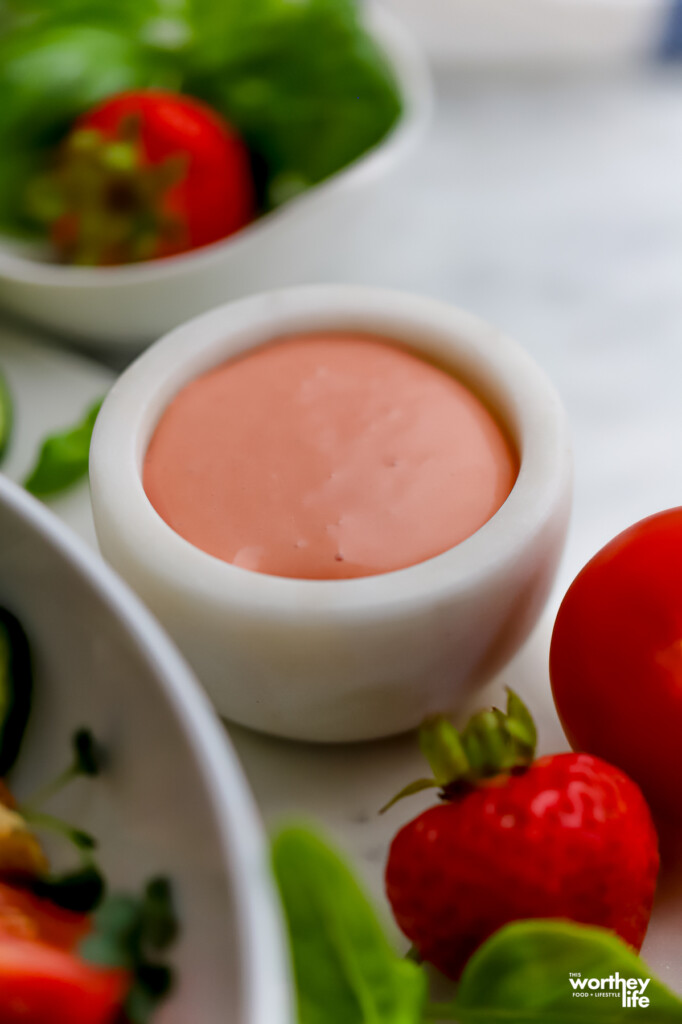 A small white marble serving container filled with strawberry vinaigrette.