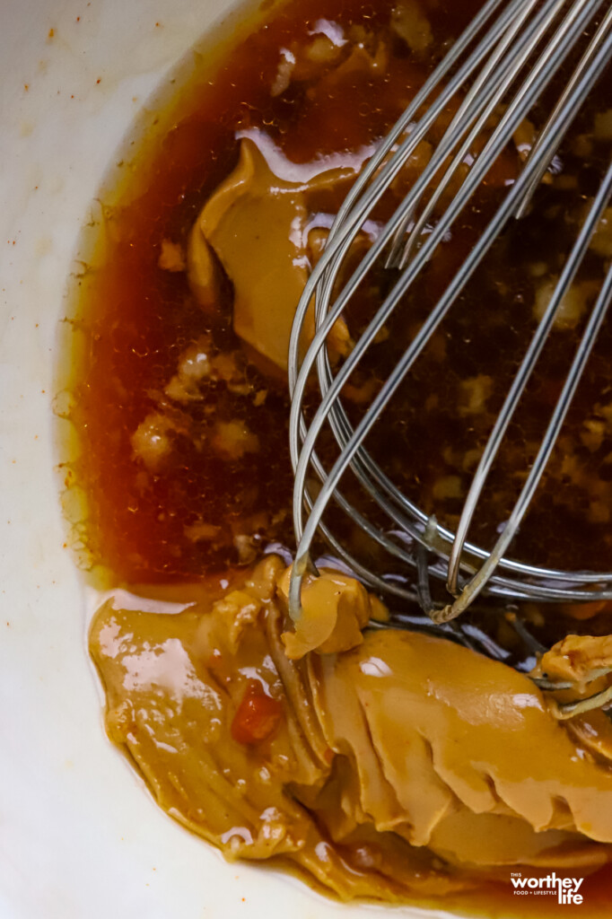 Ingredients for making Thai Cabbage Salad dressing in a white mixing bowl and a wire whisk. 