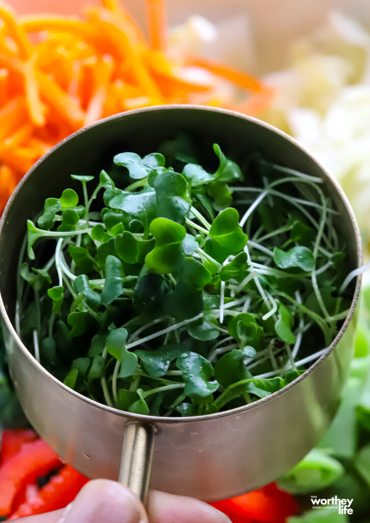 Micro greens in a brass colored measuring cup.