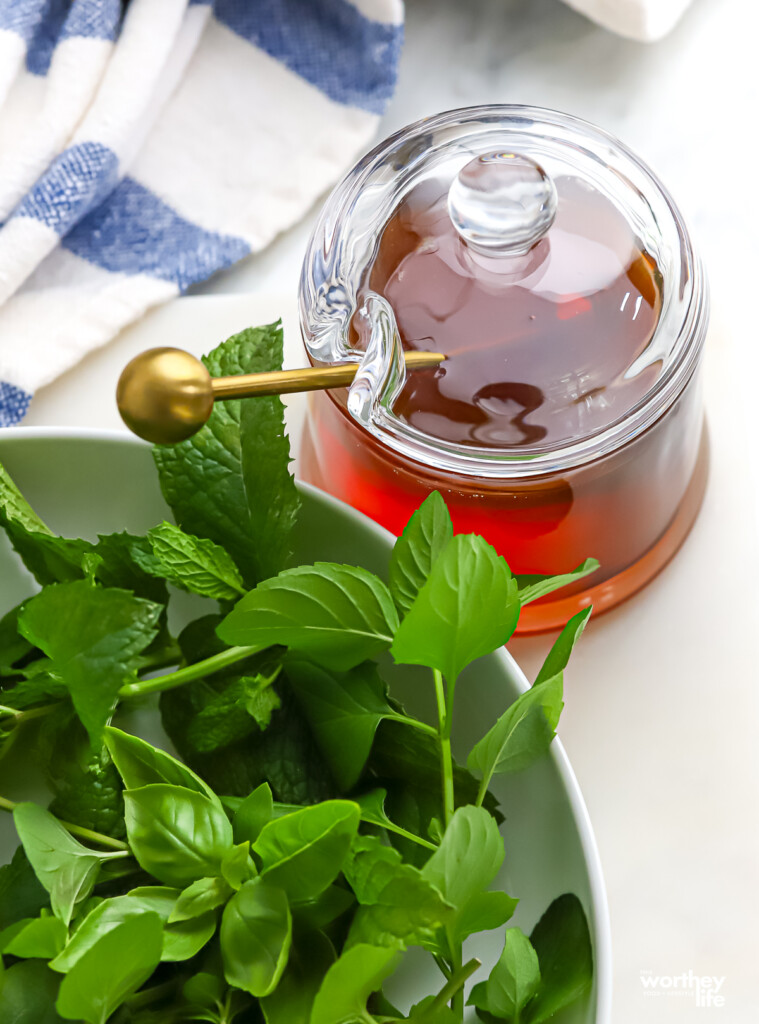  a while bowl filled with sweet basil, lemon basil and mint, and a jar of honey.