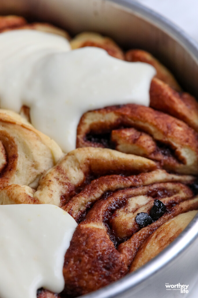 Partially iced blueberry cinnamon rolls in a cake pan.