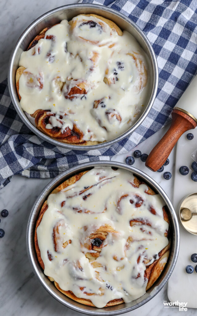 Two pans of our blueberry cinnamon rolls with a checkered apron.