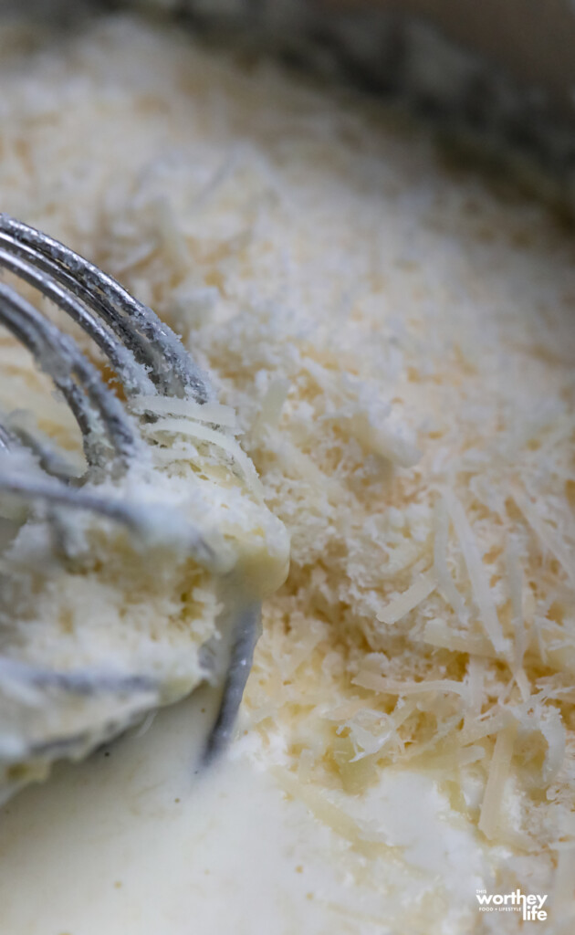 A sauce pot with heavy cream and grated cheeses