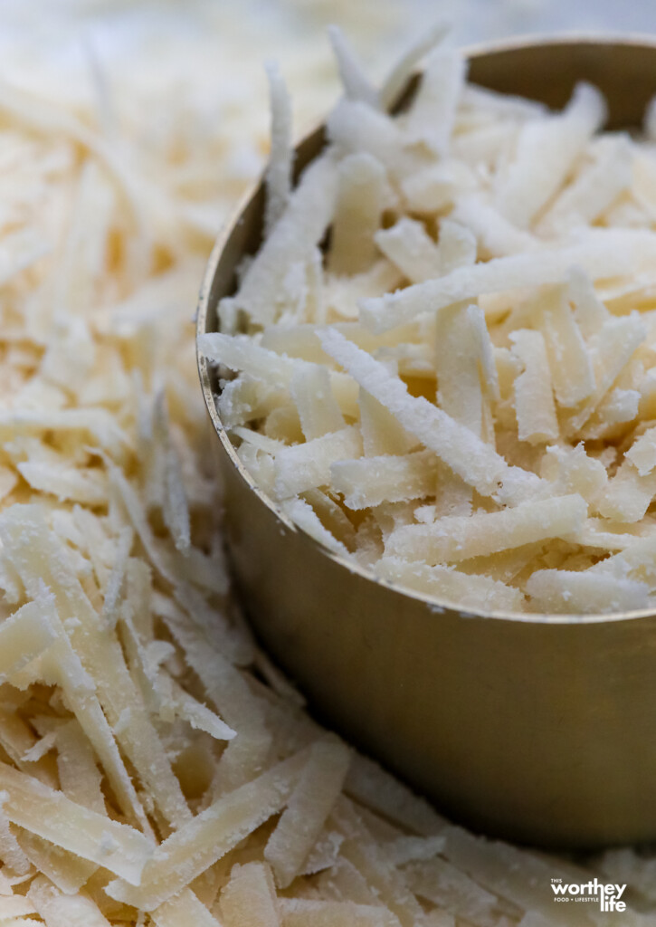 A brass measuring cup filled with grated Italian cheese. 