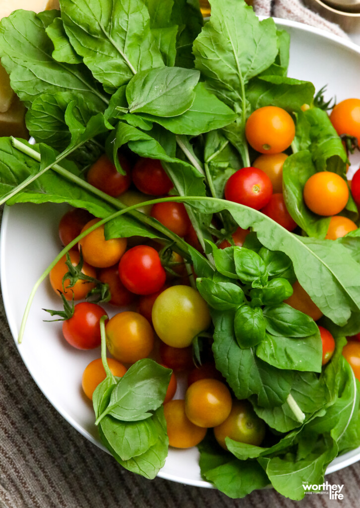 A white platter with arugula, cherry tomatoes, and sweet basil