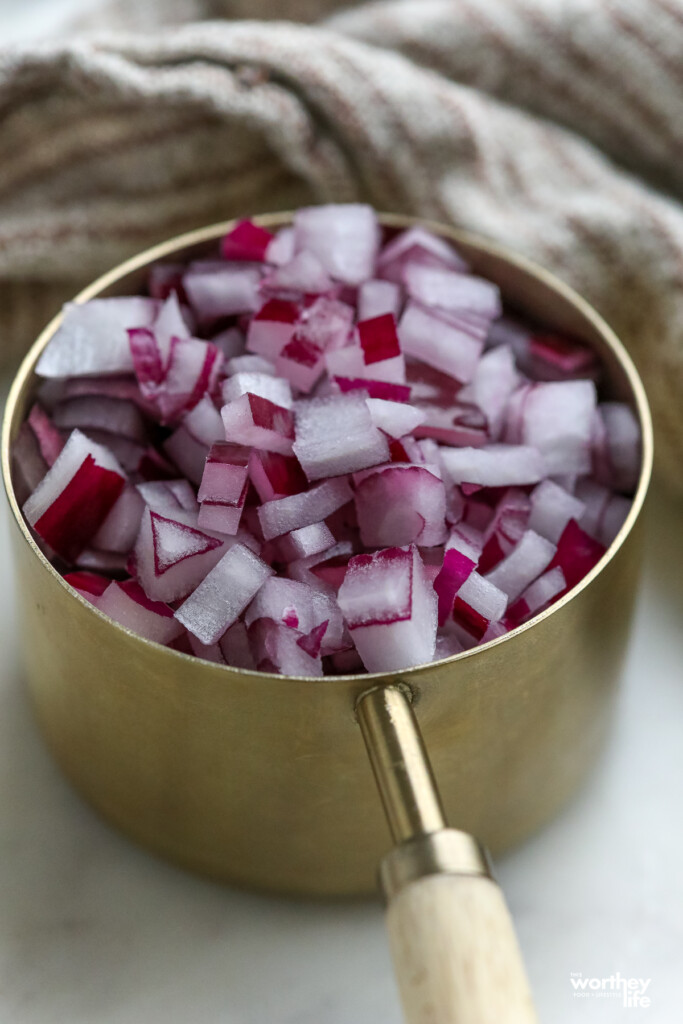 Chopped onions in measuring cup on marble cutting board