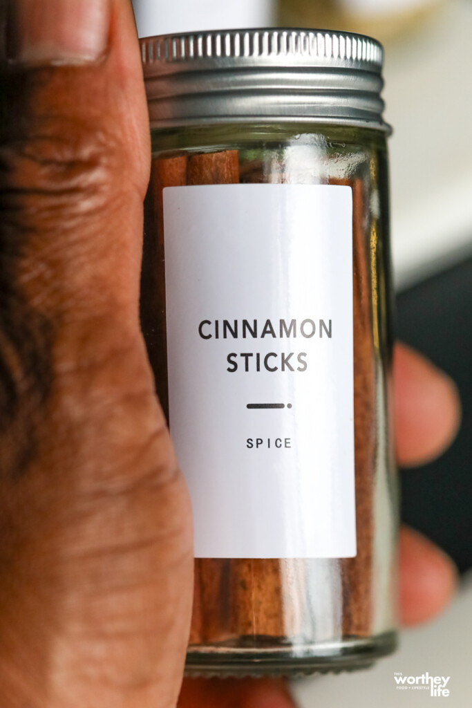  A hand hold a clear glass container with cinnamon sticks.