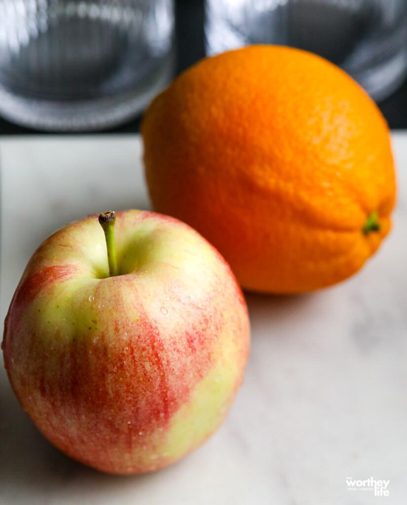  An apple and orange on a white marble cutting board. 