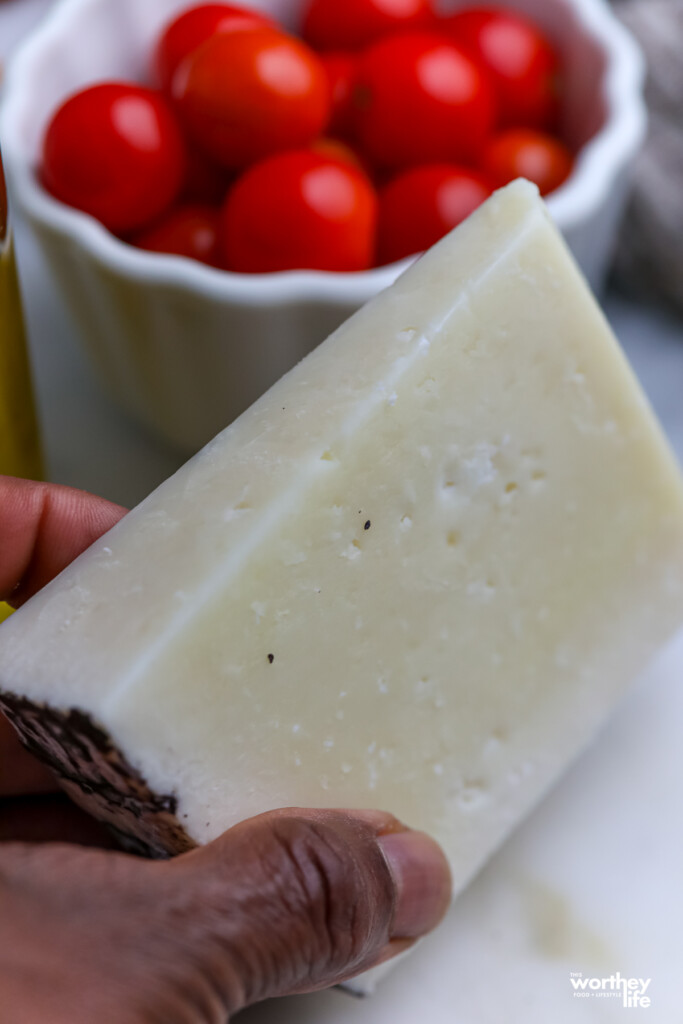  A wedge of pecorino romano cheese and a bowl of fresh cherry tomatoes in the background.