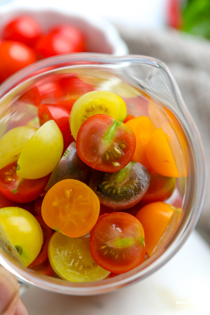 A glass measuring cup filled with half slices of cherry tomatoes.