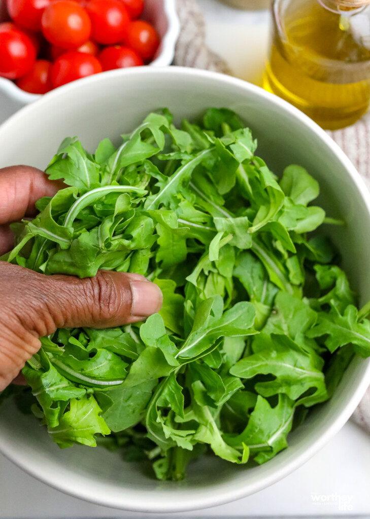 A white salad bowl filled with fresh arugula. 