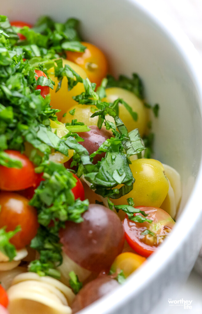 A large white bowl filled with pasta, tomatoes, chopped arugula and sweet basil. 