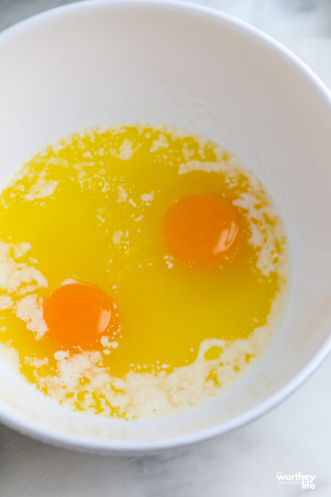 A medium white bowl with melted unsalted butter and fresh farm eggs.