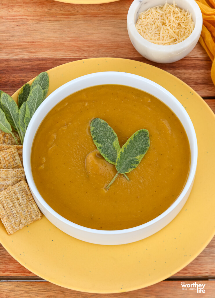 A white bowl filled with Butternut Acorn Squash Soup with crackers and a small bowl of cheese