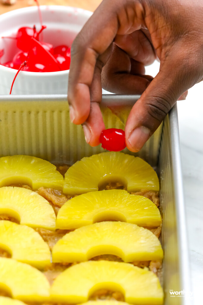 man's hand adding cherries to pineapple cake