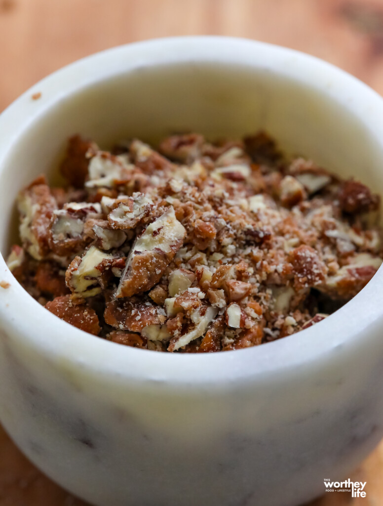 chopped praline pecans in white marble bowl