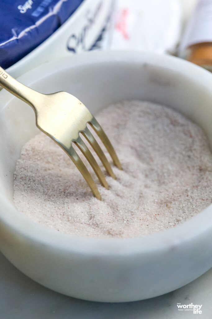 fork sifting through cinnamon sugar in a white marble bowl