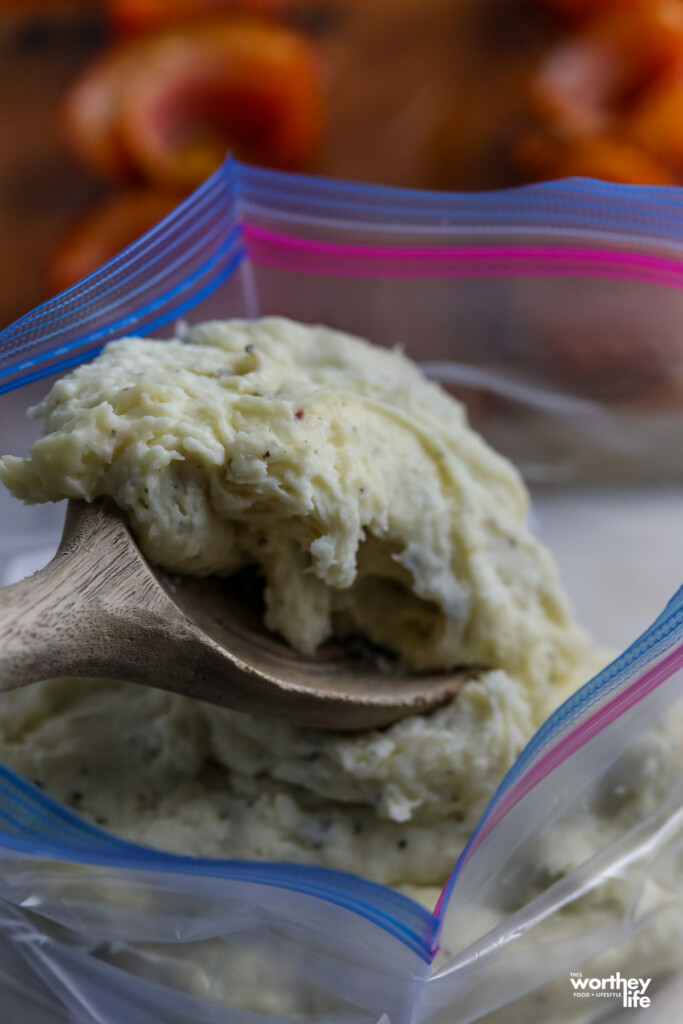 a wooden spoon with mashed potatoes going into a ziploc bag