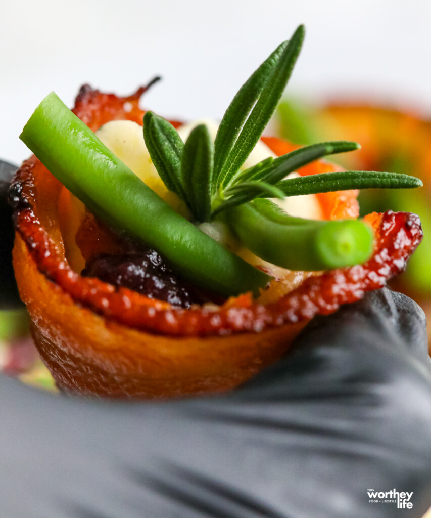 a man holding a bacon appetizer with green beans