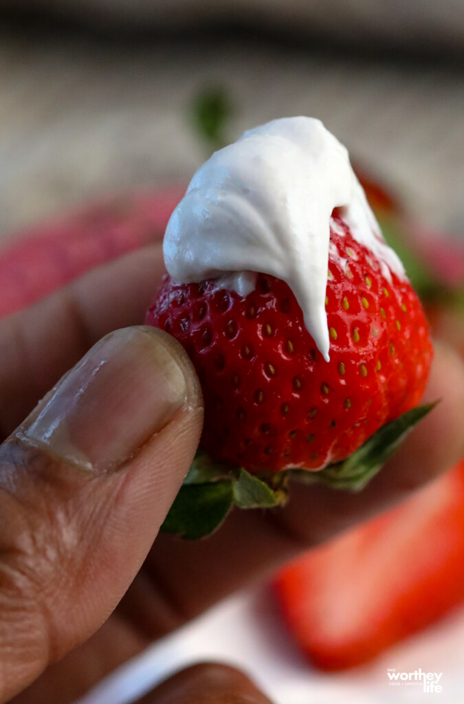 man holding a fresh strawberry with cool whip dip on it
