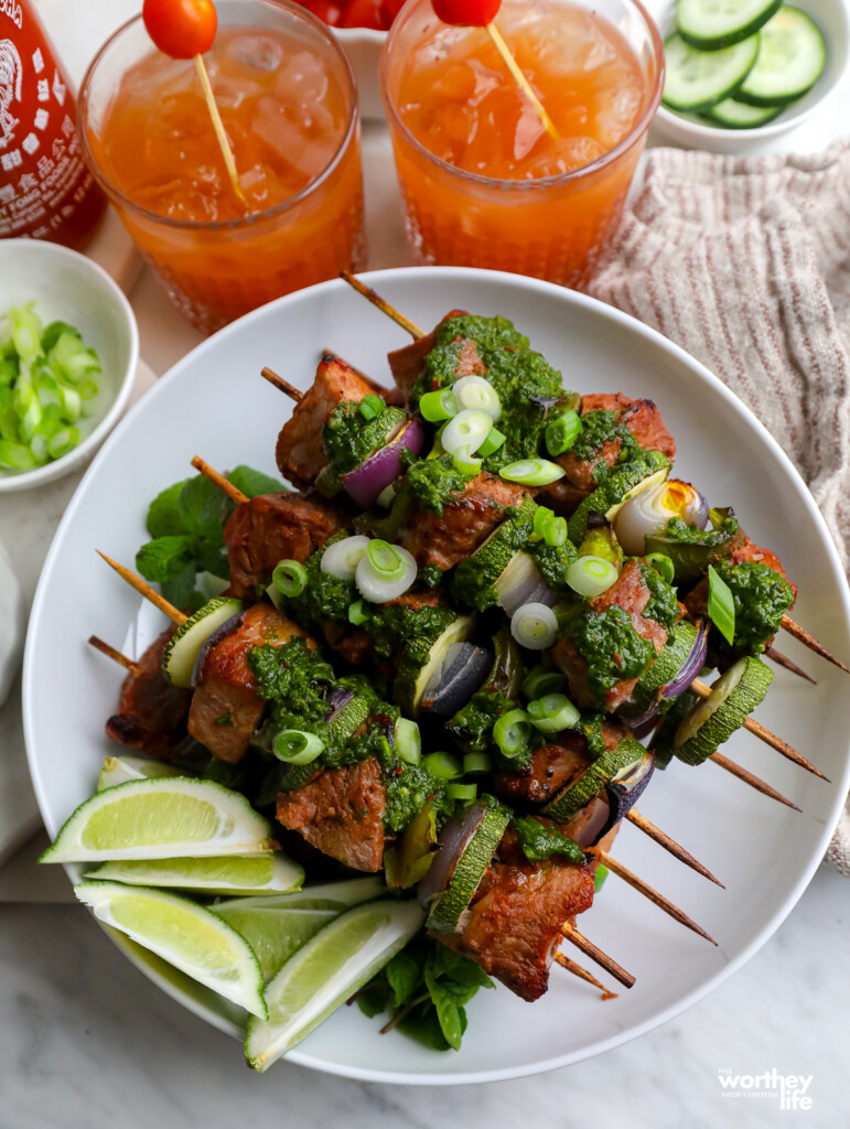 a plate of pork kabobs with vegetables on white plate