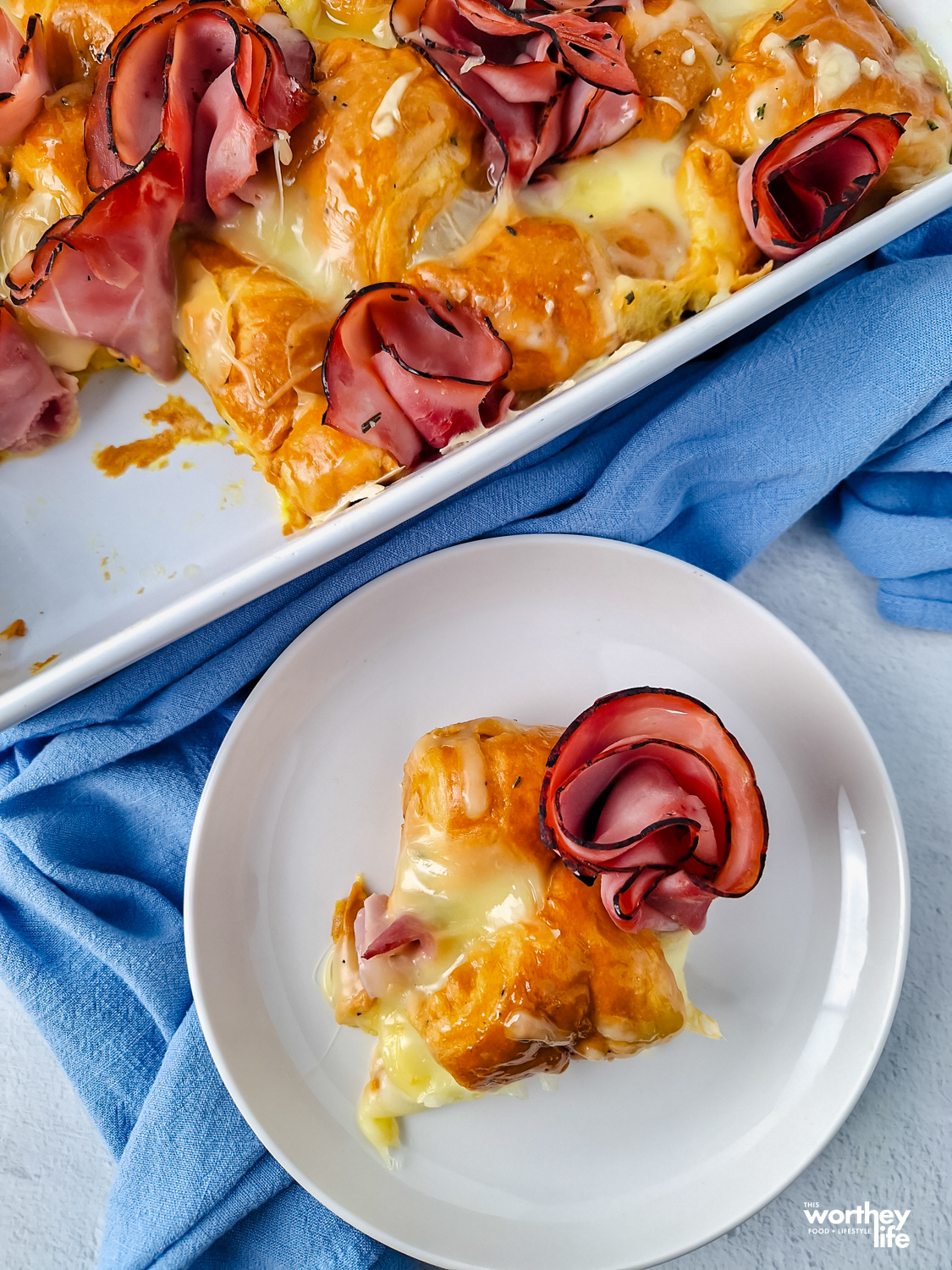 a piece of a cheesy croissant on a white plate with a blue cloth napkin