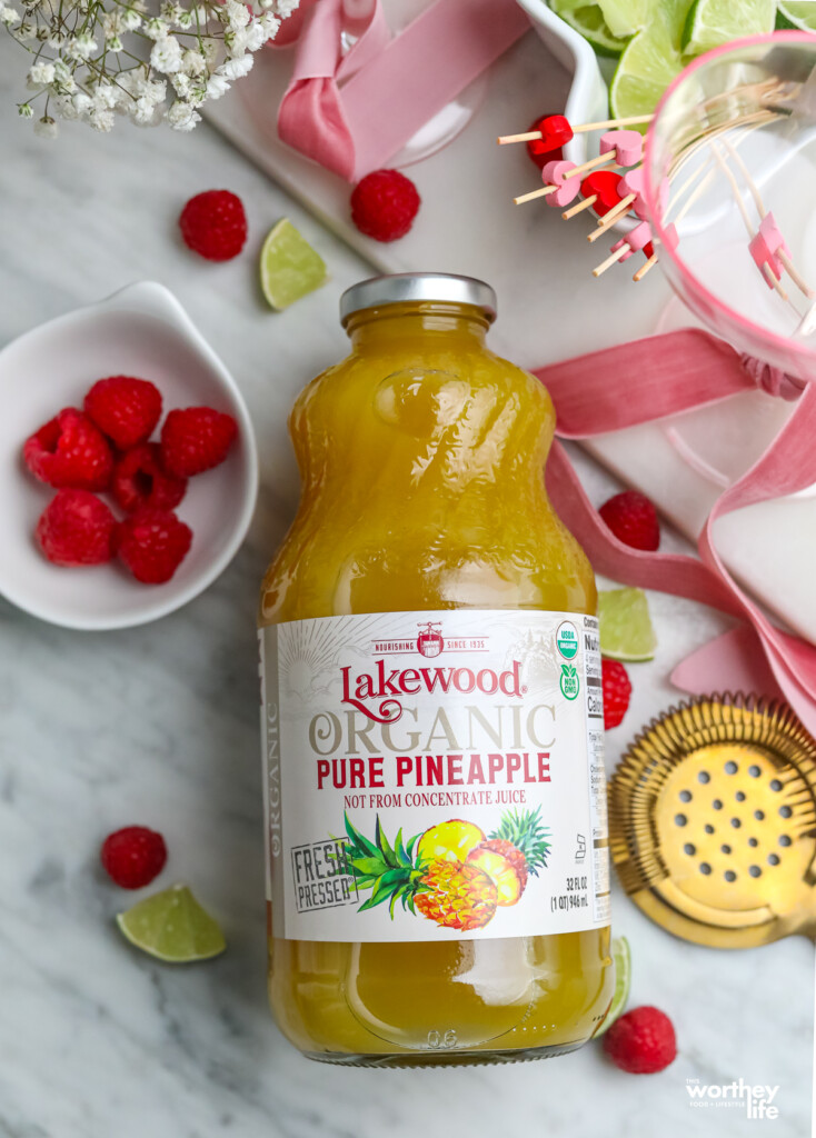 A bottle of organic pineapple juice with other ingredients to make our raspberry flavored cocktail. 